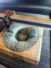 Decorative wooden box with a glass lid featuring engraved patterns, held open by a tool.