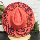 Pink cowboy hat with black floral pattern on a white tiled floor.