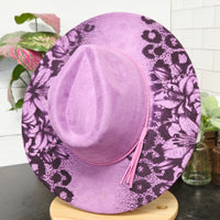 Purple floral-patterned sun hat on a white surface with greenery
