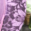 Close-up of a purple fabric with black floral pattern and pink tassel.
