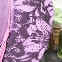Close-up of a purple fabric with black floral pattern and pink tassel.