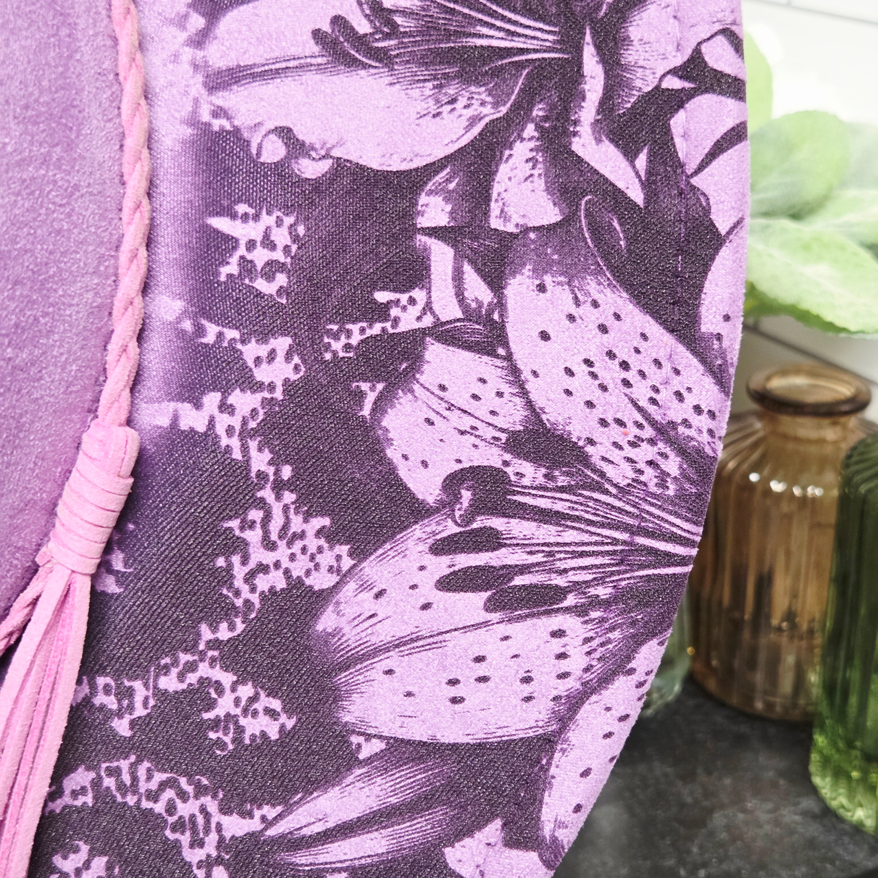 Close-up of a purple fabric with black floral pattern and pink tassel.
