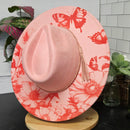 Pink hat with red floral and butterfly pattern on a light wooden surface.