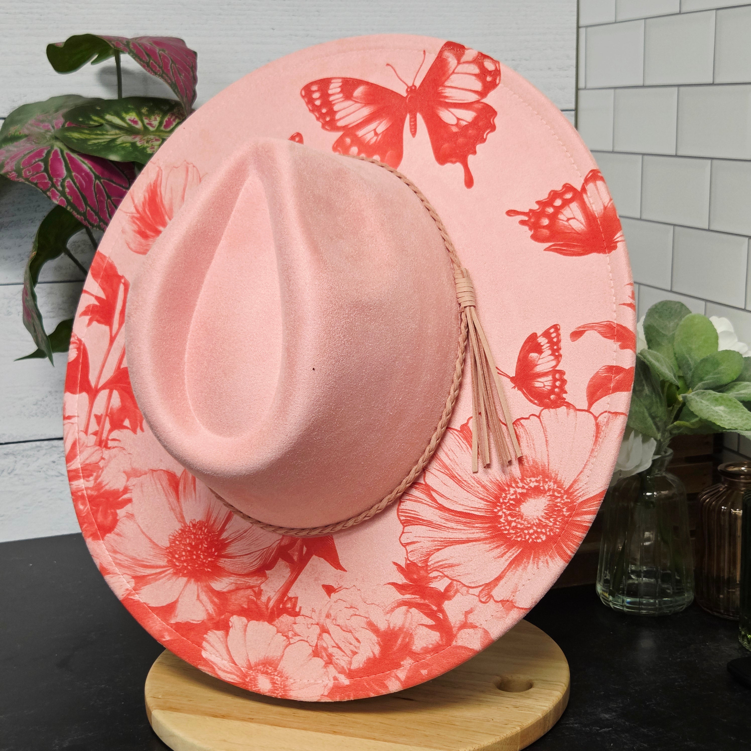 Pink hat with red floral and butterfly pattern on a light wooden surface.