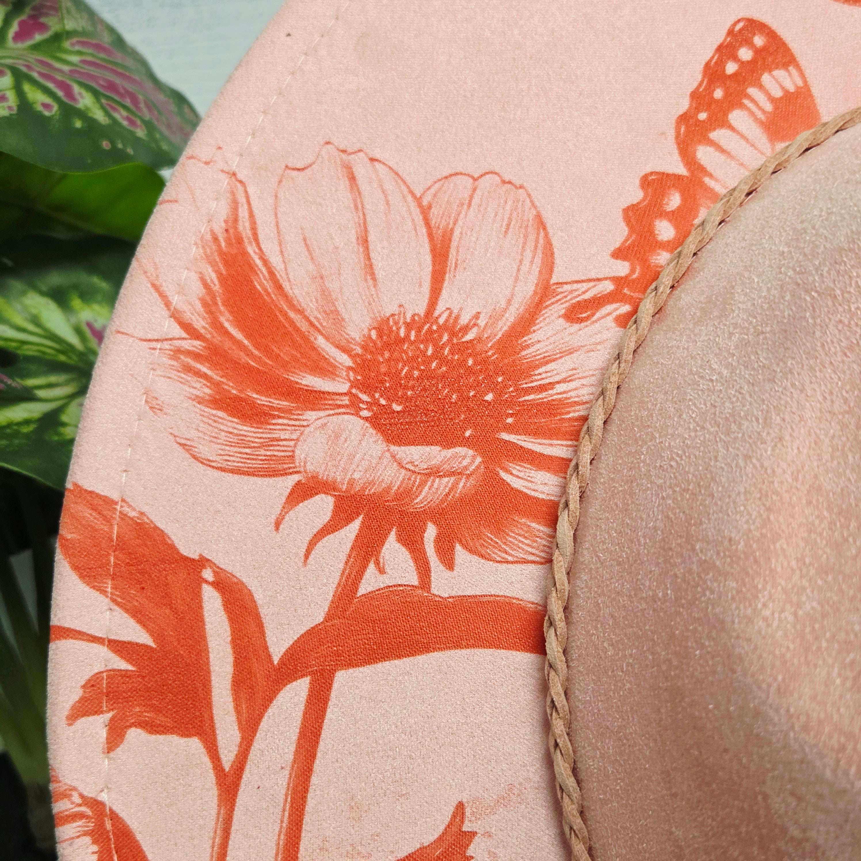 Close-up of a beige hat with orange floral design and butterfly on a light pink background.